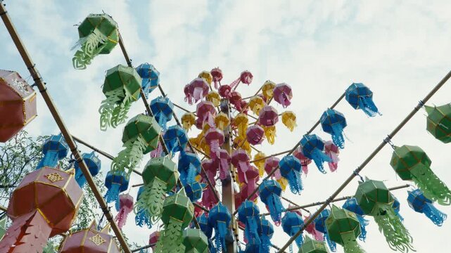 Low angle shot of a traditional light blue and gold Lanna paper lantern hanging outdoors against trees and sky in Chiang Mai, Thailand, during Yi Peng lantern festival celebrations.