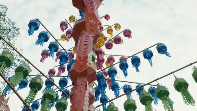 Low angle shot of a traditional light blue and gold Lanna paper lantern hanging outdoors against trees and sky in Chiang Mai, Thailand, during Yi Peng lantern festival celebrations.