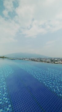Rooftop infinity swimming pool on a modern condominium in Chiang Mai, Thailand, featuring blue mosaic tiles, poolside patio, scenic cityscape, and mountain views under a daytime sky.