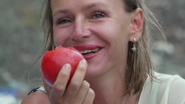 Woman biting into a juicy red tomato outdoors during a summer afternoon picnic. Close-up portrait shot.