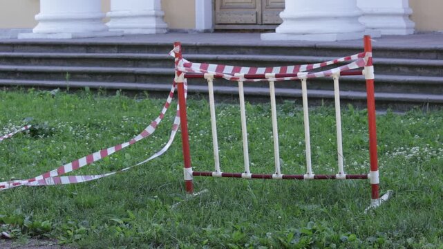 A portable plastic barrier with red vertical posts and white slats stands on a lush green lawn scattered with tiny white flowers