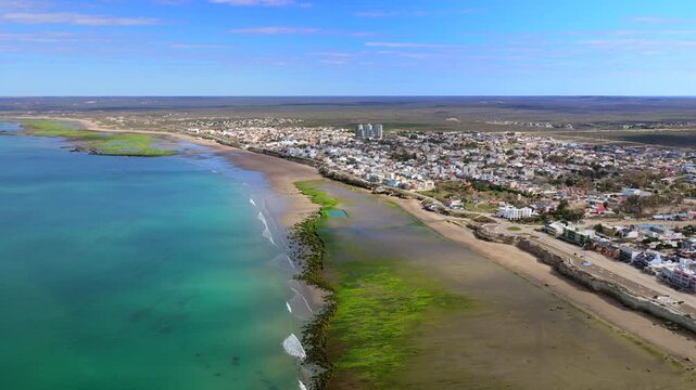 Las Grutas coastal shoreline with turquoise Golfo San Matias, broad tidal flats, sandy beach, waterfront development and Ruta Provincial 2, Rio Negro, drone forward flyover