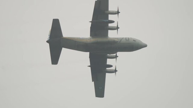 Underside tracking shot of Greek military transport plane displaying anniversary livery while maneuvering overhead during Falcon Leap airborne operation commemoration near Oosterbeek.