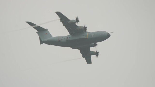 German Air Force military transport aircraft maneuvers overhead through overcast grey sky during international Falcon Leap tactical paratrooper exercise in Gelderland Netherlands.