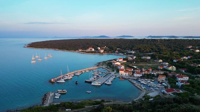 A stunning aerial drone shot capturing the warm golden sunset over the Sotorisce bay and Mulj harbor area on Silba Island, Croatia. The perspective showcases the sheltered marina filled with boats