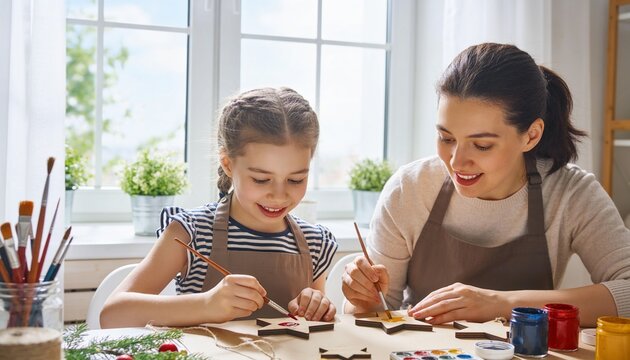 Mother and daughter painting wooden star ornaments at home table, preparing handmade Christmas decorations and enjoying creative family time