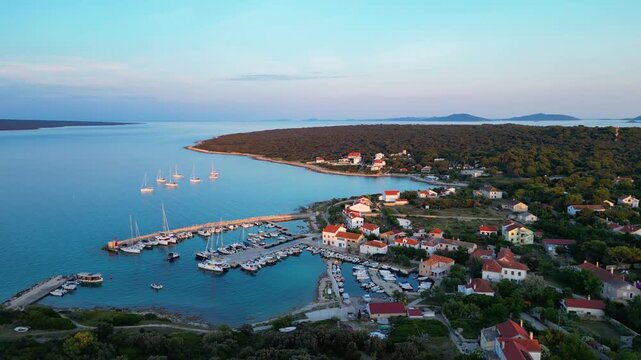 A stunning aerial drone shot capturing the warm golden sunset over the Sotorisce bay and Mulj harbor area on Silba Island, Croatia. The perspective showcases the sheltered marina filled with boats