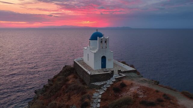 Scenic drone shot of the traditional Greek whitewashed chapel on a cliff above the Mediterranean at sunrise, church of the Seven Martyrs on Sifnos island, holiday in the Cyclades, Greece
