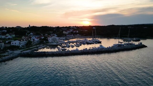 A stunning aerial drone shot capturing the warm golden sunset over the Sotorisce bay and Mulj harbor area on Silba Island, Croatia. The perspective showcases the sheltered marina filled with boats