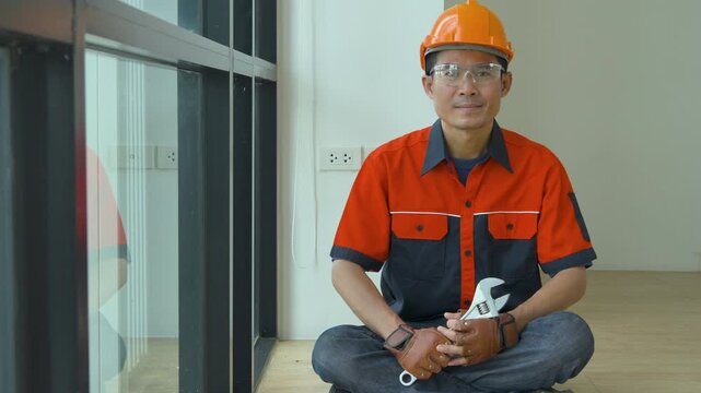 Professional construction worker sitting on the floor holding a large adjustable metal wrench