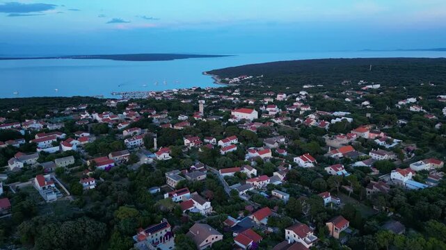 A breathtaking evening aerial drone panorama of old village on Silba Island, Croatia. The shot showcases the vibrant turquoise harbor, a docked ferry, and the charming coastal village stretching