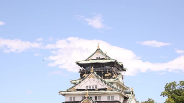 View of the iconic main tower of Osaka Castle in Japan, showcasing traditional Japanese castle architecture surrounded by greenery beneath a bright sky.