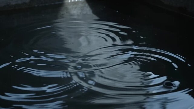 Raindrops making ripples on the dark water of a storage tank