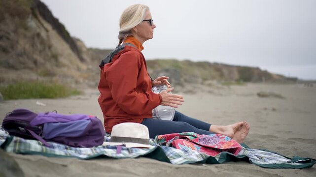 Senior woman plays a drum while sitting on the sand at Fort Bragg beach in Mendocino, California, enjoying the coastal setting.