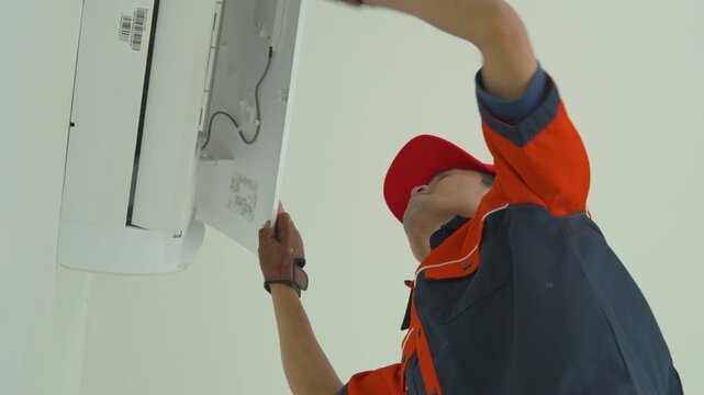Professional technician in uniform performing maintenance on a wall mounted air conditioner unit