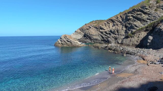 Discover the serene charm of La Frana Beach in Sardinia, Italy. Crystal-clear waters gently lap at the shore while a couple enjoys the peaceful atmosphere surrounded by stunning cliffs.