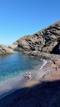 A couple experience a beautiful day at La Frana Beach in Sardinia, Italy, where soft waves meet pebbly shores and sun-kissed cliffs. Enjoy the serene atmosphere perfect for relaxation and fun.
