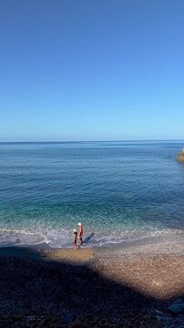 A couple bask in the beauty of La Frana Beach, Sardinia, Italy, where crystal-clear waters meet soft pebbles. Enjoy the serene atmosphere and breathtaking coastal scenery.