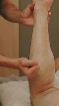 close-up view of hands holding raised forearm and applying thumb pressure near elbow in warm indoor therapy