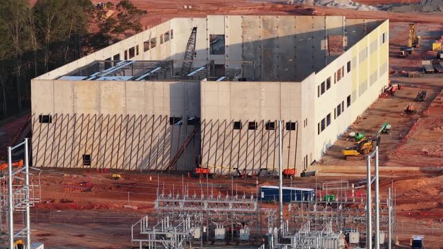Tilt up concrete data hall with a two story window bank and a crawler crane inside stands over the steel bus work of the adjoining substation in Louisa County, Virginia. Aerial view