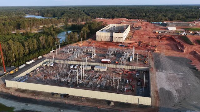 Sound walled substation and control building serve a data center campus in Louisa County, Virginia, surrounded by graded red clay, stormwater ponds and unbroken pine forest. Aerial wide shot
