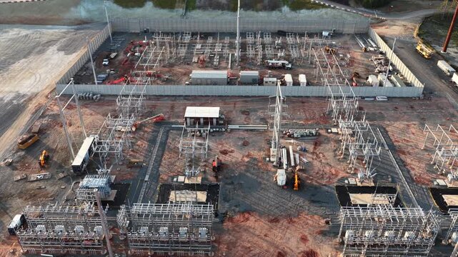 Steel bus structures, transformers and cable trenches fill a new substation yard in Louisa County, Virginia, where crews and service trucks work inside the precast sound wall. Aerial view