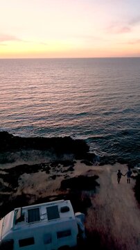 A couple experiences breathtaking beauty as the sun sets over La Frana Beach in Sardinia, Italy. Waves gently crash against the shore, creating a tranquil atmosphere perfect for relaxation