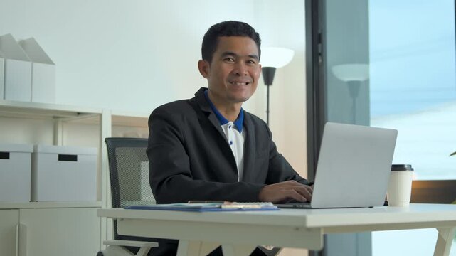 Professional man in a black blazer working on a laptop at a bright modern office workstation