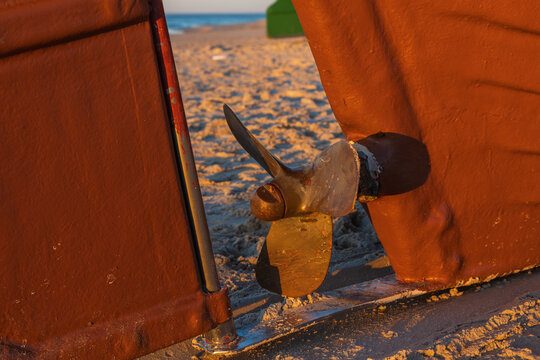 Bronze boat propeller framed between rudder and hull on sandy sunset beach