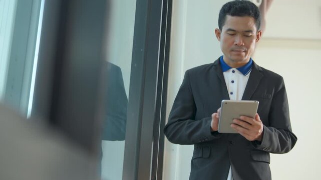 Professional man in a suit jacket using a digital tablet while standing near a glass window