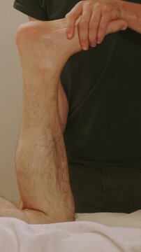 therapist cradles heel and supports calf during seated foot exam, with white towel under limb in clinical room