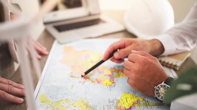 Renewable energy engineer pointing at world map and show colleagues planned location for new wind farm, discussing global expansion, clean power infrastructure and sustainable energy development