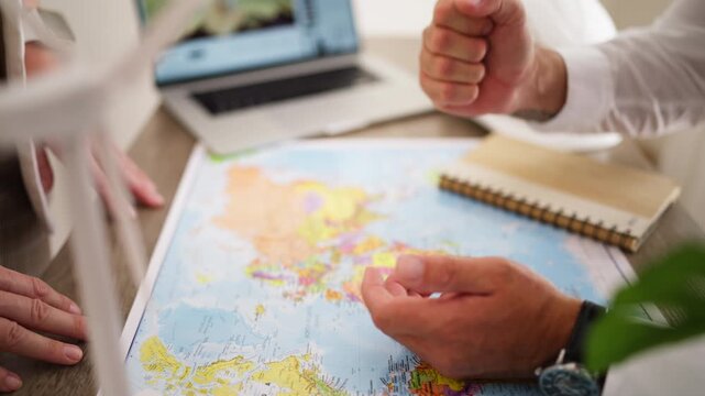 Two engineers discussing a new renewable energy project, pointing at a world map to plan the global placement of wind turbines for sustainable power generation in their modern office