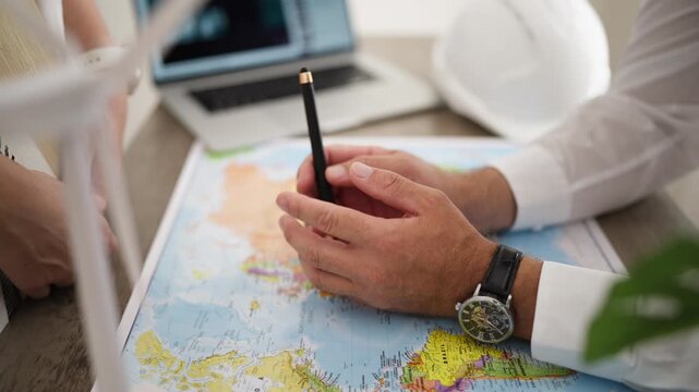 Engineer identifying location on map for wind farm project, explaining site planning to colleagues and discussing turbine deployment, renewable power generation and large-scale energy infrastructure