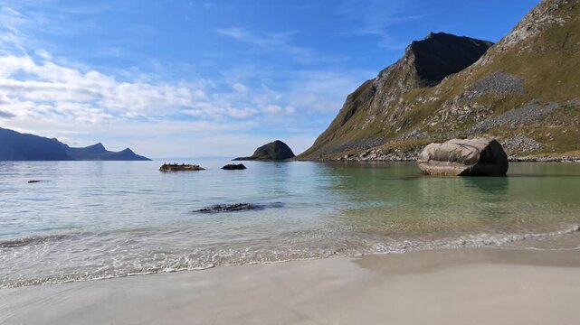 Summer landscape at Haukland Beach in the Lofoten Islands with pale sandy beach, shallow water, impressive mountains and blue sky with white clouds.