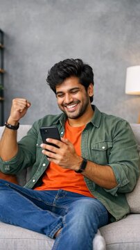 Happy young man celebrating success on his smartphone in a living room