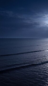 Dark deep blue ocean at night under moody moonlight, tranquil calm water surface with ripples