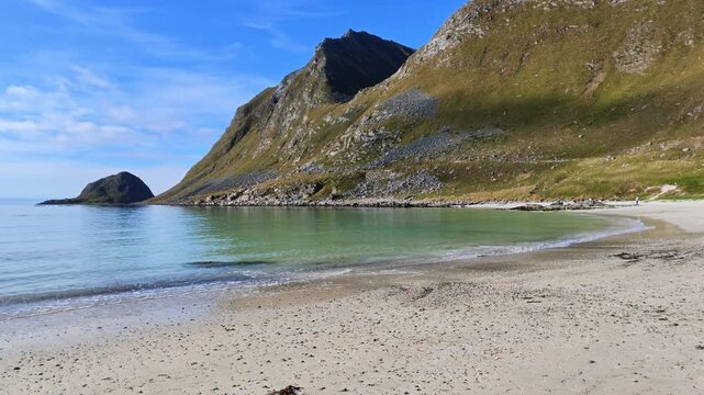 Summer landscape at Haukland Beach in the Lofoten Islands with pale sandy beach, shallow water, impressive mountains and blue sky with white clouds.