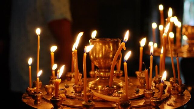 Many thin beeswax candles burning on a circular metal stand inside a dark church interior. Slow motion