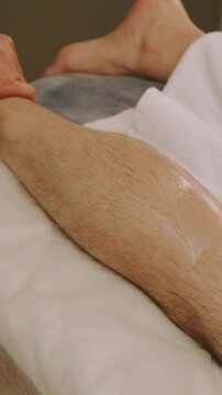 closeup view of therapist hands applying firm thumb pressure and gliding strokes on oily hairy calf warm light