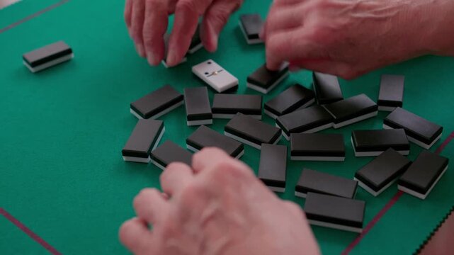 People playing dominoes shuffling tiles on green table
