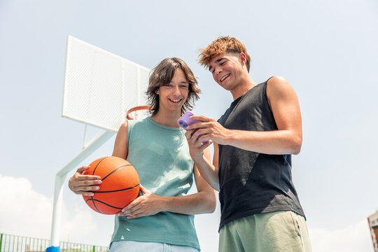 Multicultural friends checking smartphone on basketball court