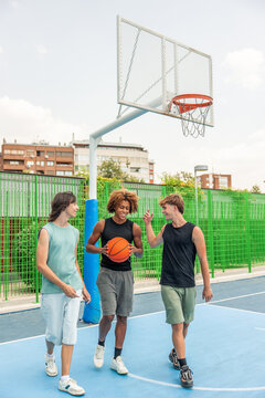 vertical Multicultural young friends walking on basketball court talking