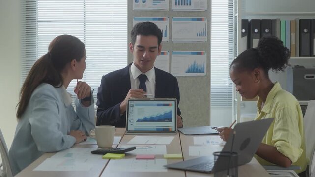 A diverse business team reviews performance data together, with printed analytics boards visible in the background of a bright, well-organized workspace.	