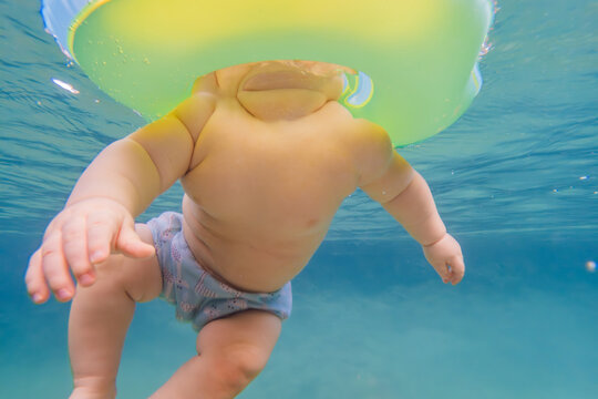 Cute baby swimming with neck float ring underwater in pool. Infant water activities, early development, wellness and happy childhood concept with family care and safety