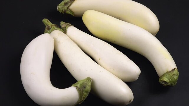 White fresh eggplants are on the black table, side view