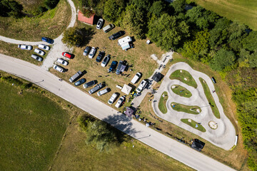 Fototapeta premium A wide aerial view of the asphalt pumptrack park in Zagorje ob Savi, Slovenia, surrounded by green fields, rolling hills, a railway line, and a bright blue sky filled with fluffy white clouds.