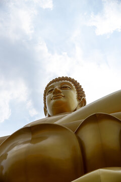 Head and shoulders of the giant golden Buddha at Wat Paknam against a bright sky