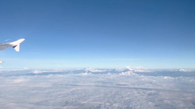 Aerial view from an airplane over the Ecuadorian mountain range, revealing the majestic peaks of the Antisana, Cotopaxi, and Ilinizas volcanoes emerging through a blanket of clouds.