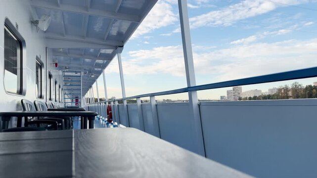 An open cruise ship deck glides smoothly along the Neva River. Tables and chairs invite passengers to relax under the bright blue sky. The calm atmosphere brings a peaceful and joyful feeling.